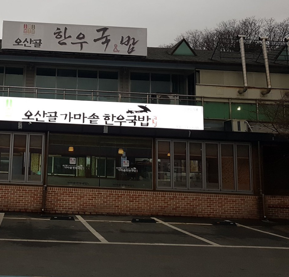 해 질 녘 매장 앞 주차장과 불 켜진 ‘오산골 가마솥 한우국밥’ 간판