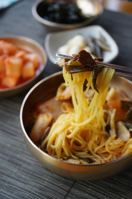 놋쇠 그릇에서 젓가락으로 든 노란 면과 소고기
